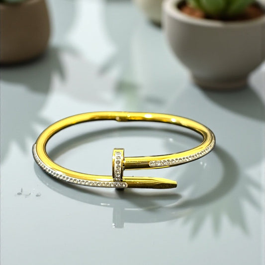 Gold Anti Tarnish bracelet on a reflective surface with potted plants in the background