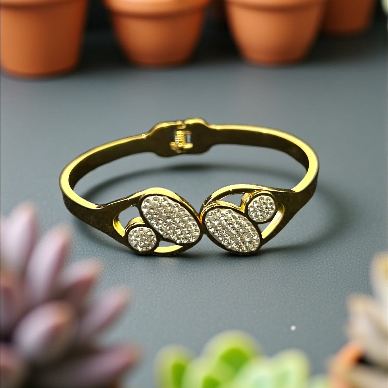 Anti tarnish Gold colour bracelet with leaf design on a gray surface with potted succulents in the background