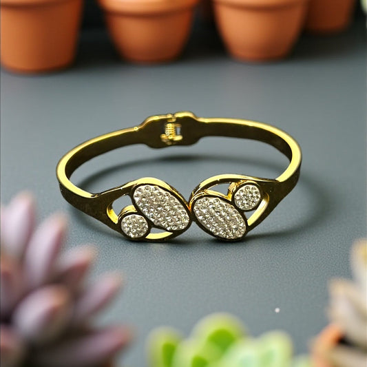 Anti tarnish Gold colour bracelet with leaf design on a gray surface with potted succulents in the background