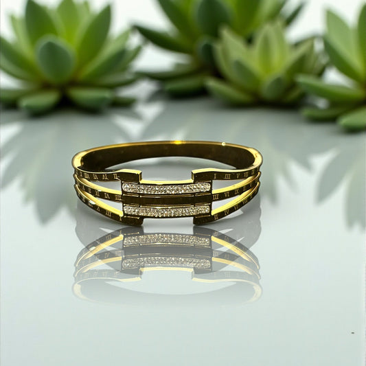 anti tarnish Gold bracelet  with diamond accents on a reflective surface with green plants in the background