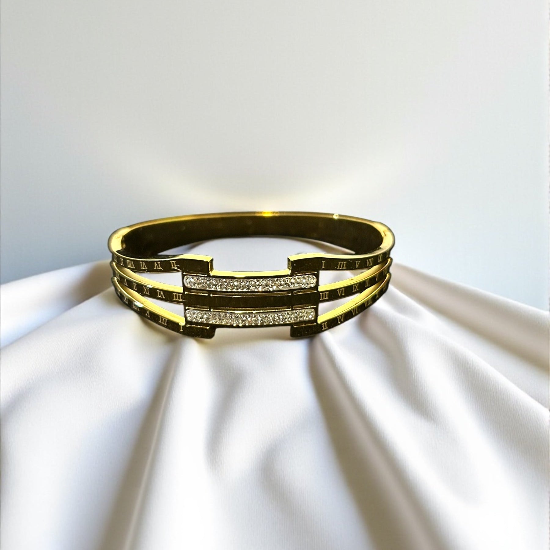 Gold bracelet with embedded stones on a white fabric background