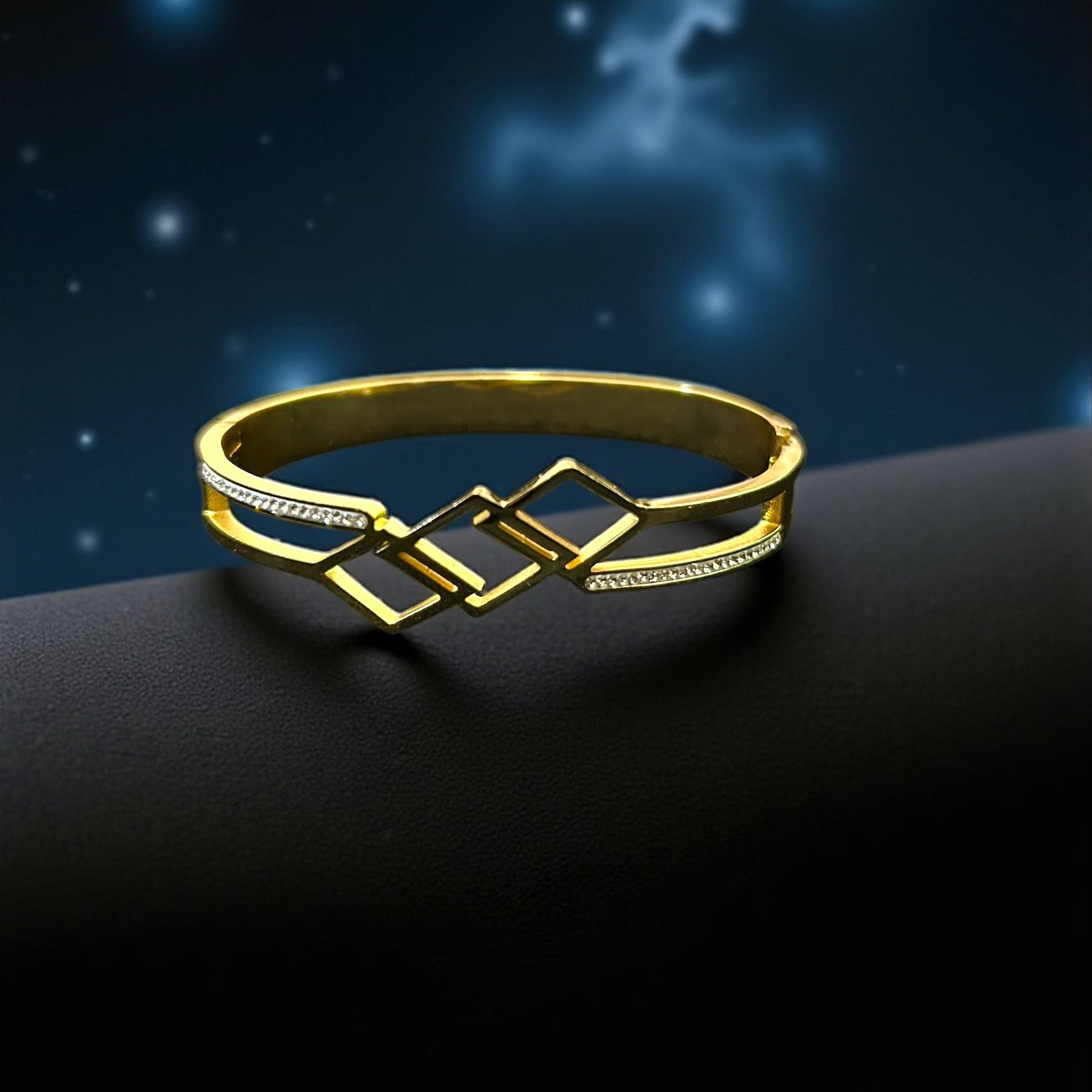 Gold bracelet on a dark surface with a starry night sky background