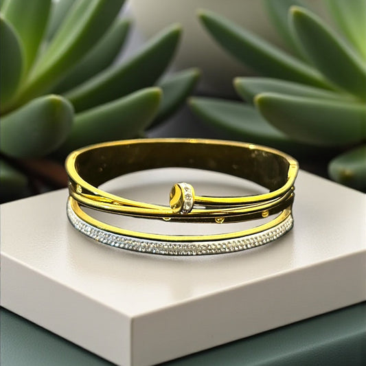  gold and silver bracelets on a white surface with green plants in the background